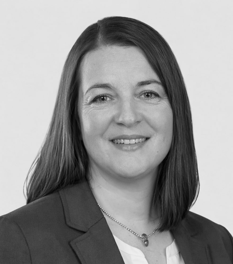Professional headshot of a smiling woman with shoulder-length dark hair, wearing a blazer and necklace.