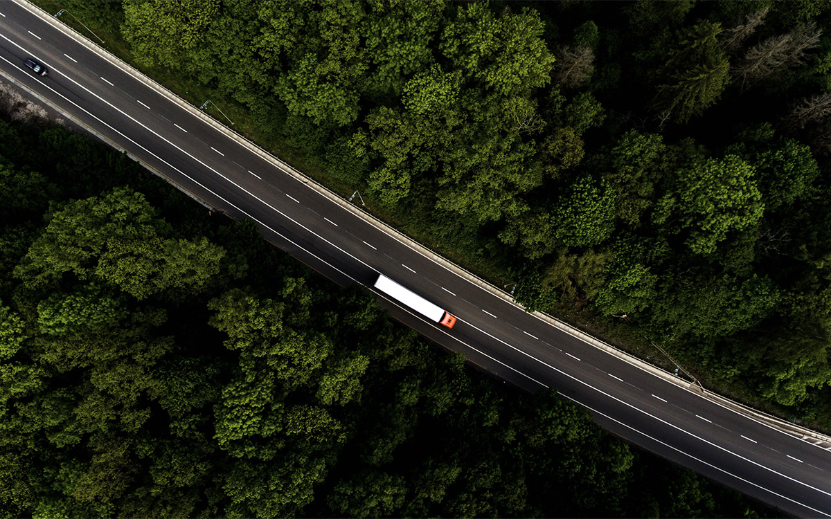 Aufnahme einer Strasse mit Elektrolastwagen und Wald von oben.